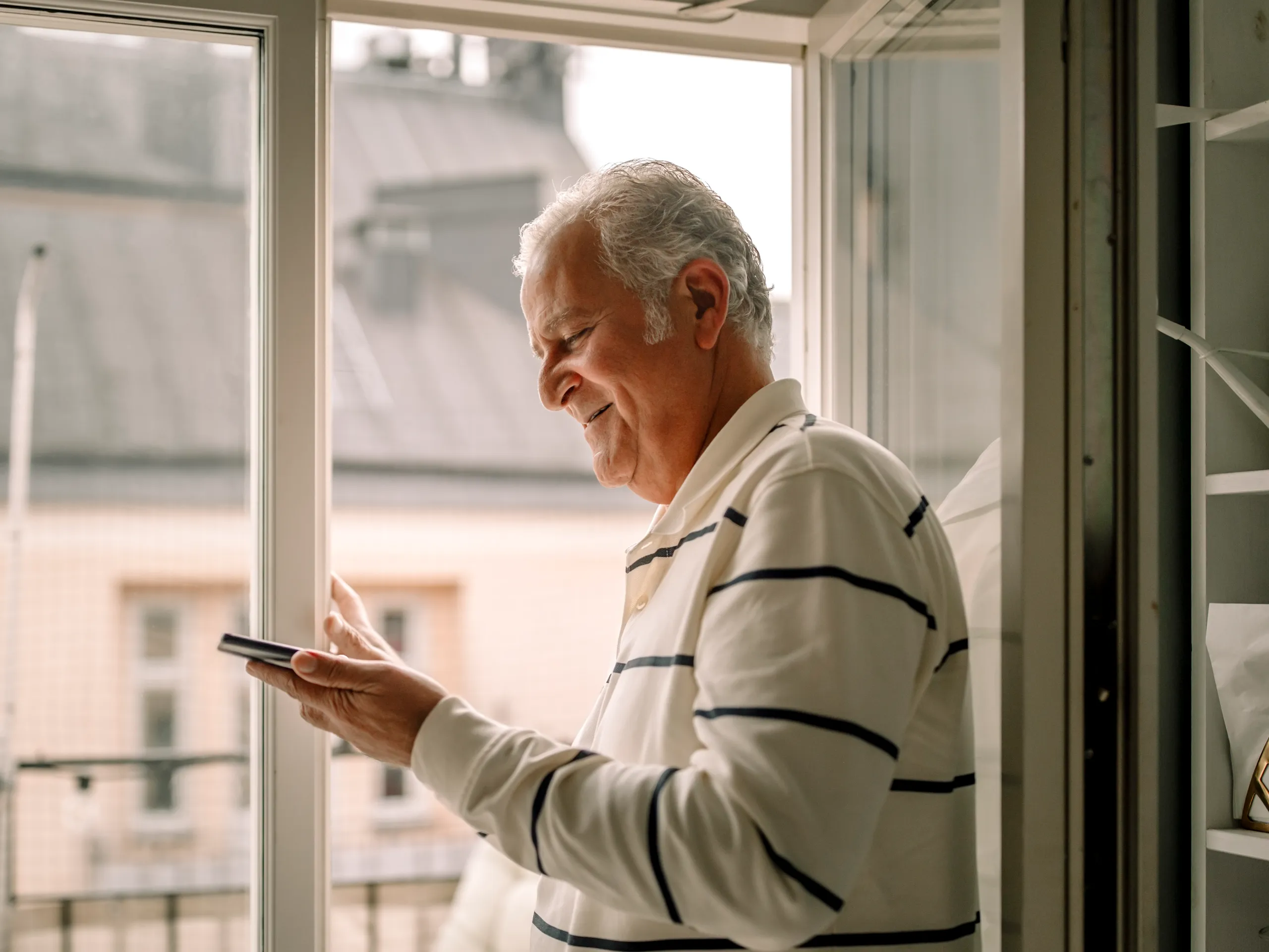 Älterer Mann nutzt ein Smartphone vor einem Fenster
