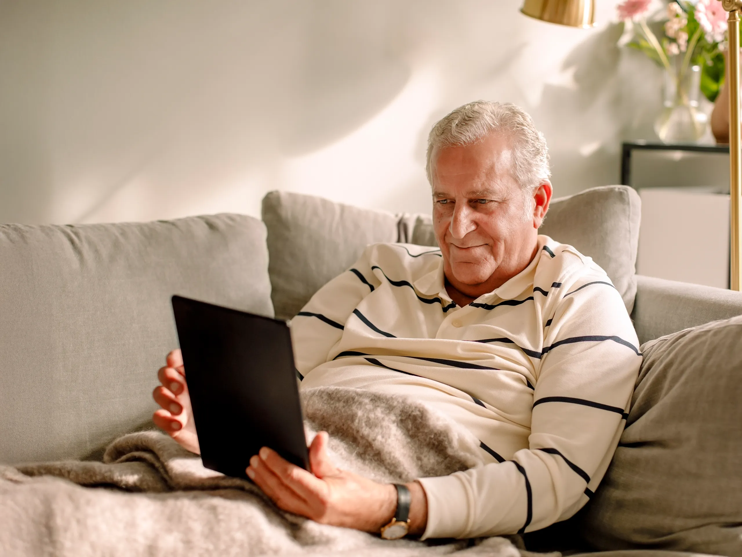 Älterer Mann sitzt entspannt auf dem Sofa und nutzt ein Tablet