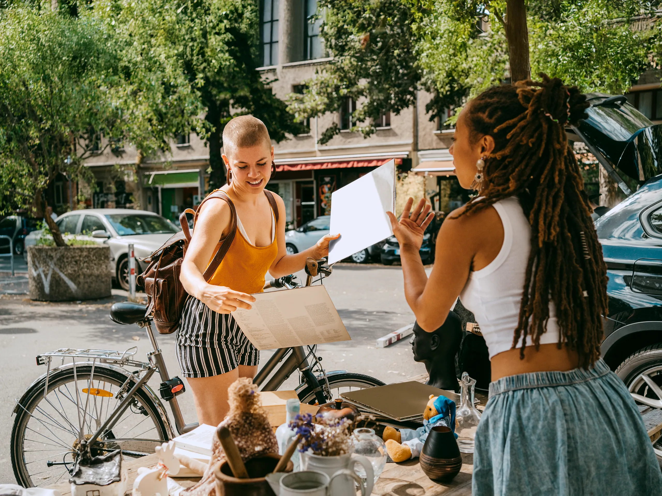 Zwei Frauen auf einem Flohmarkt, eine hält eine Schallplatte, während sie mit der anderen spricht.