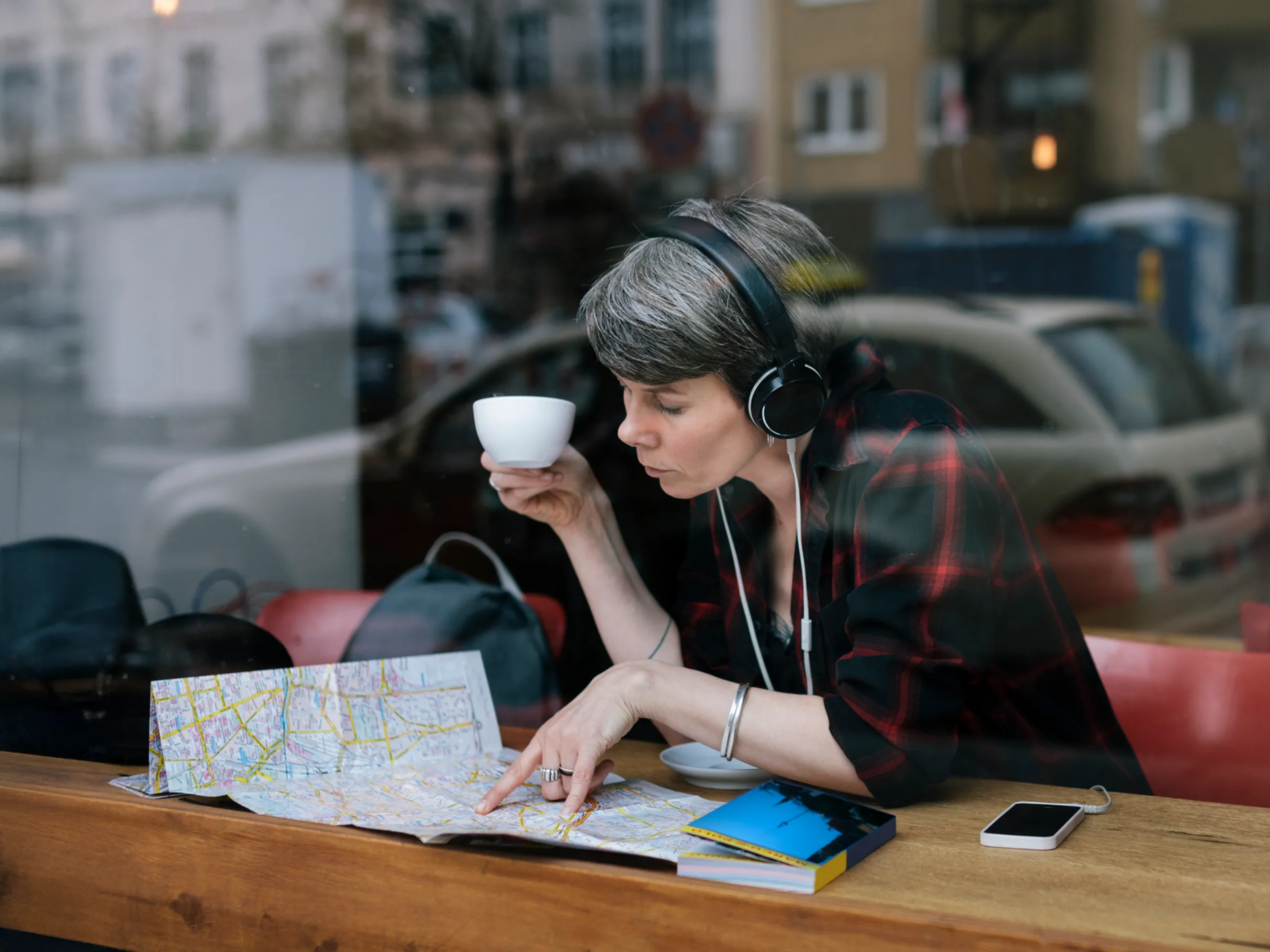 Frau mit Kopfhörern trinkt Kaffee und studiert eine Landkarte in einem Café.