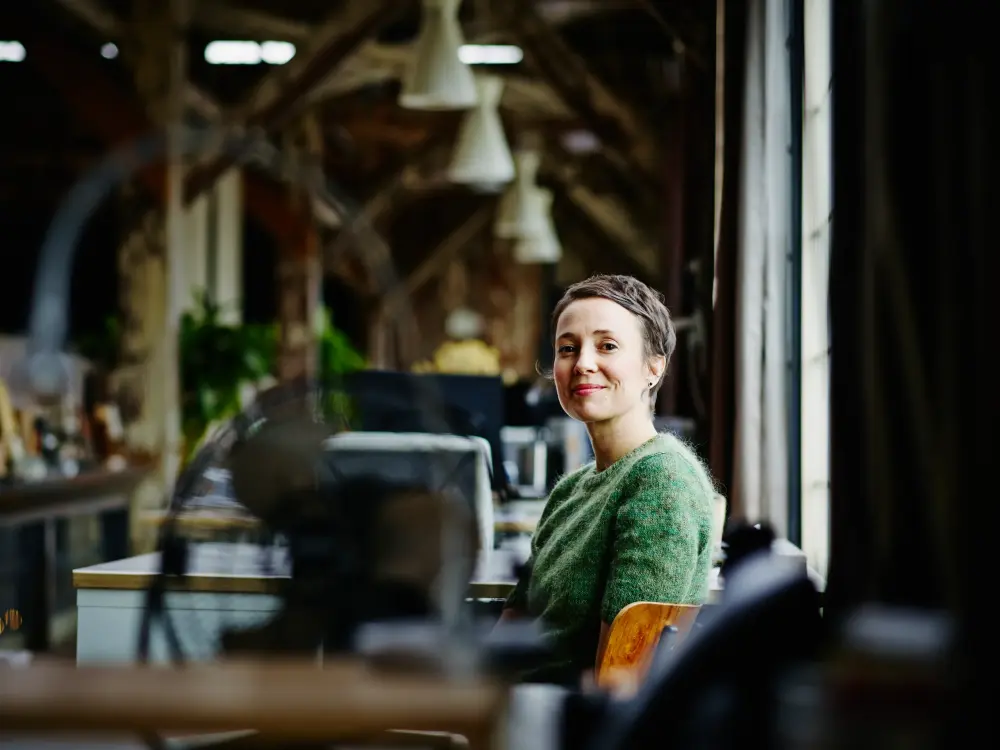 Frau in grüner Strickjacke sitzt in einem modernen Büro und lächelt