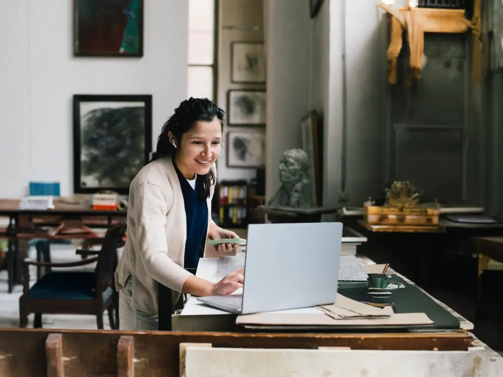 Lächelnde Frau arbeitet mit Laptop in einem kreativen Atelier.