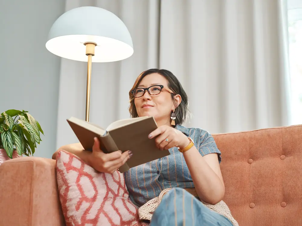 Frau liest Buch auf Sofa mit Stehlampe