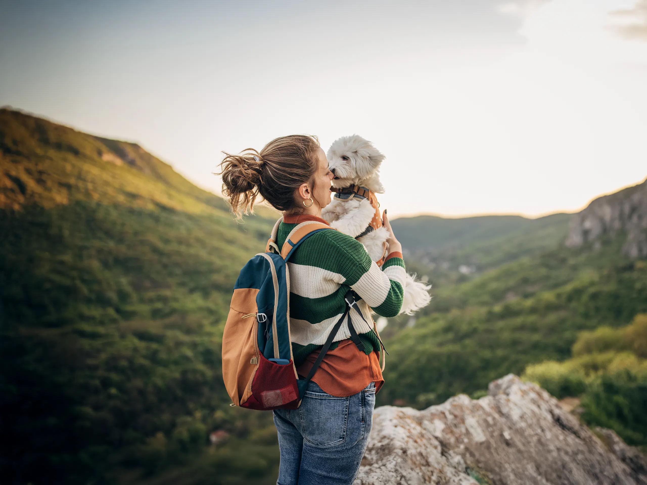 Frau küsst ihren Hund auf einem Felsen mit Blick ins Tal