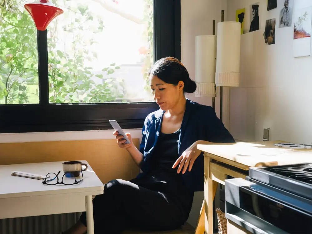 Frau sitzt entspannt in der Sonne und schaut auf ihr Smartphone.