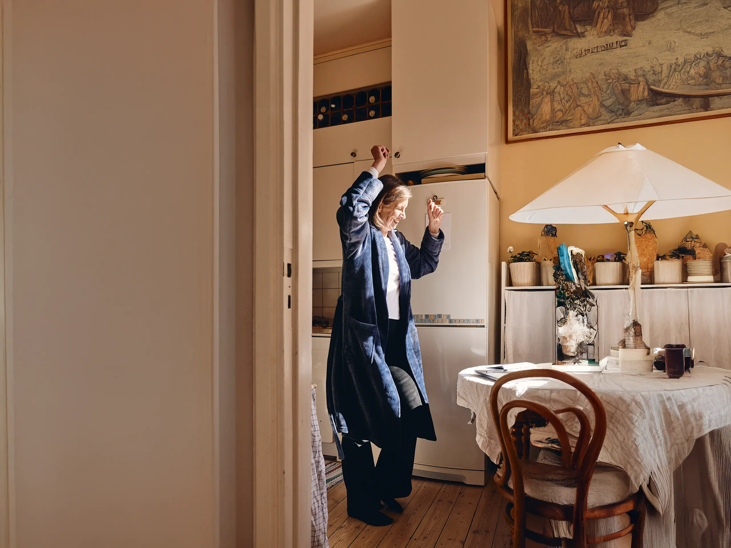 Frau tanzt fröhlich in heller Küche neben gedecktem Tisch