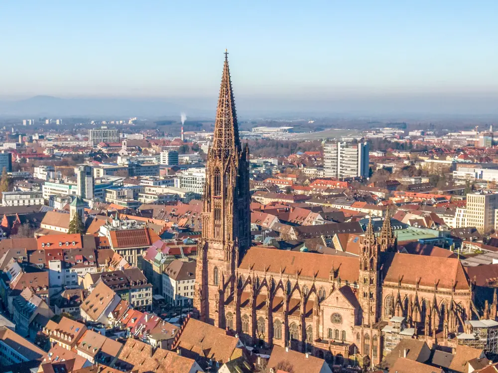 Luftaufnahme des Freiburger Münsters mit Altstadt und Schwarzwald im Hintergrund