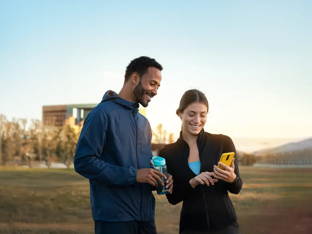 Zwei Menschen lachen beim Blick auf Smartphone nach dem Joggen