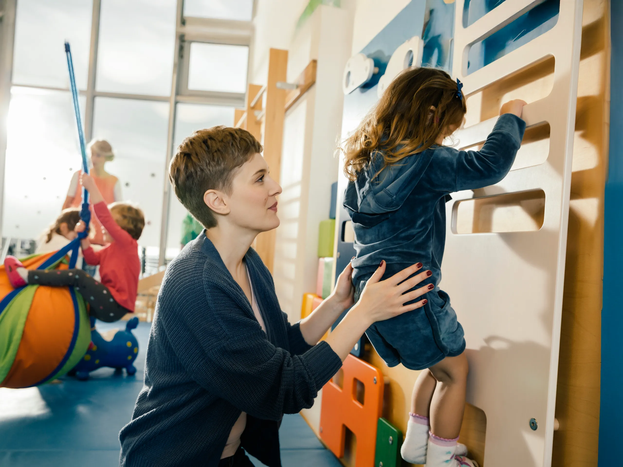Eine Betreuerin hilft einem Kind beim Klettern an einer Kletterwand in einer Kindertagesstätte.