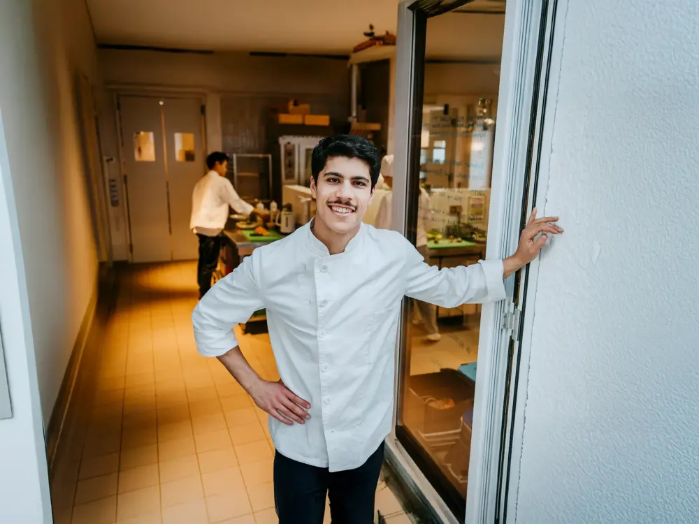 Junger Koch steht lächelnd vor Restaurantküche