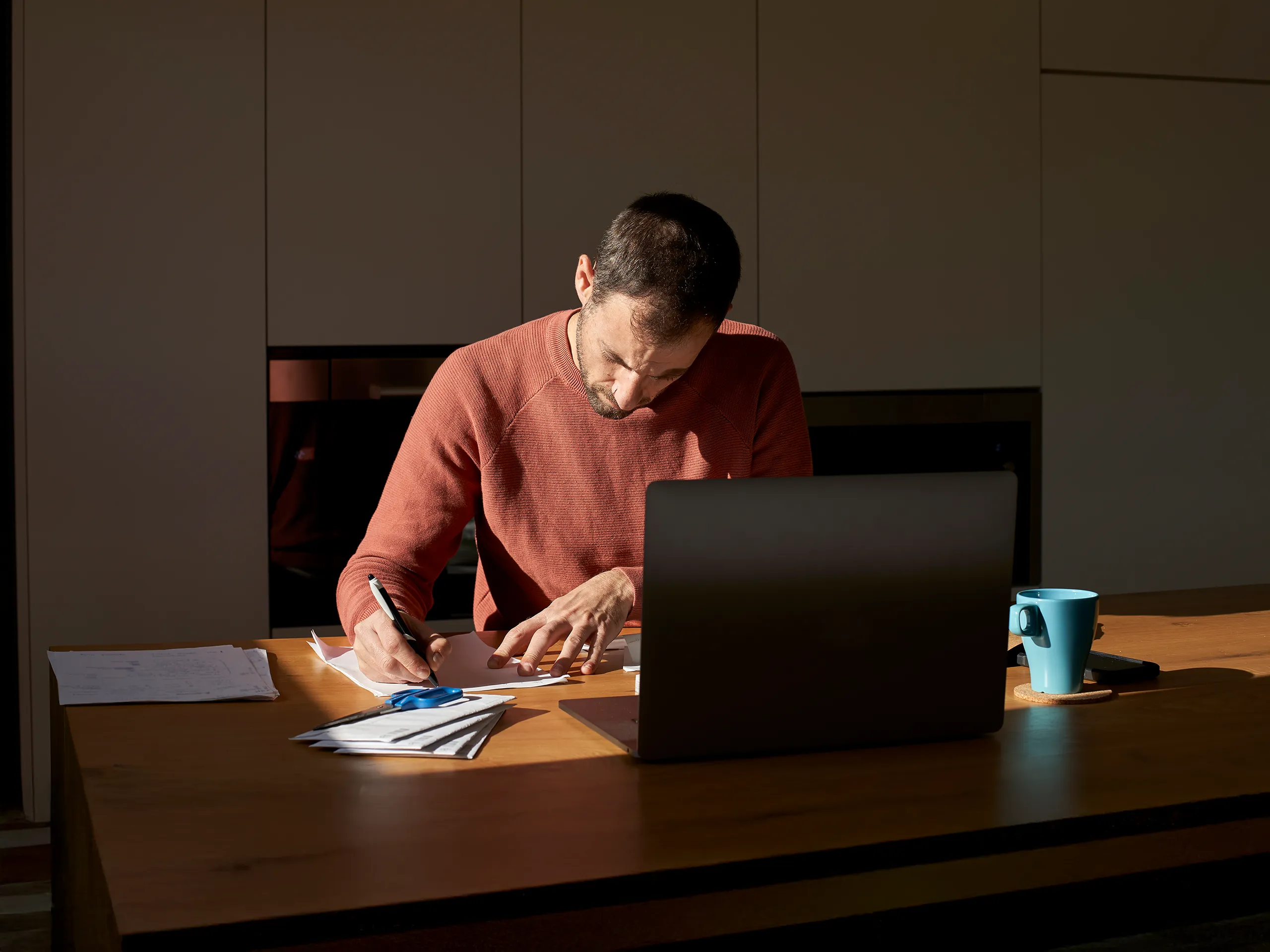 Mann arbeitet konzentriert mit Laptop und Unterlagen an einem Holztisch