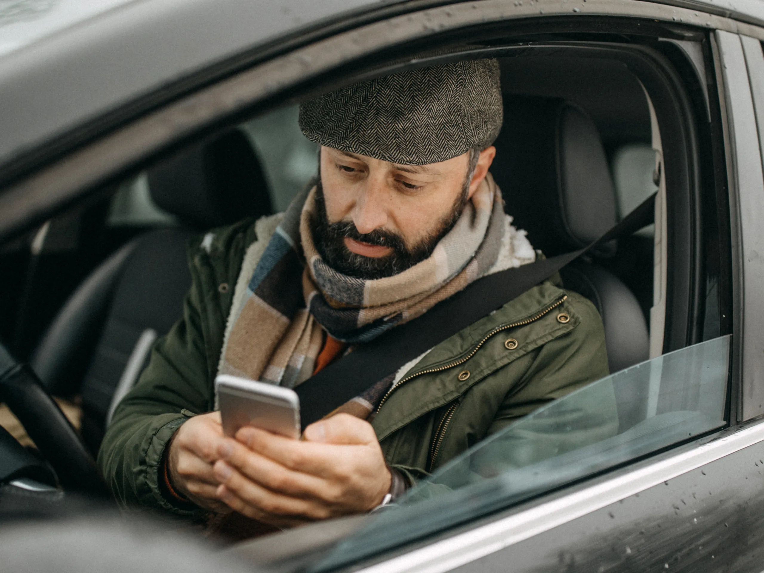 Mann im Auto, der auf seinem Smartphone tippt, während er den Sicherheitsgurt trägt