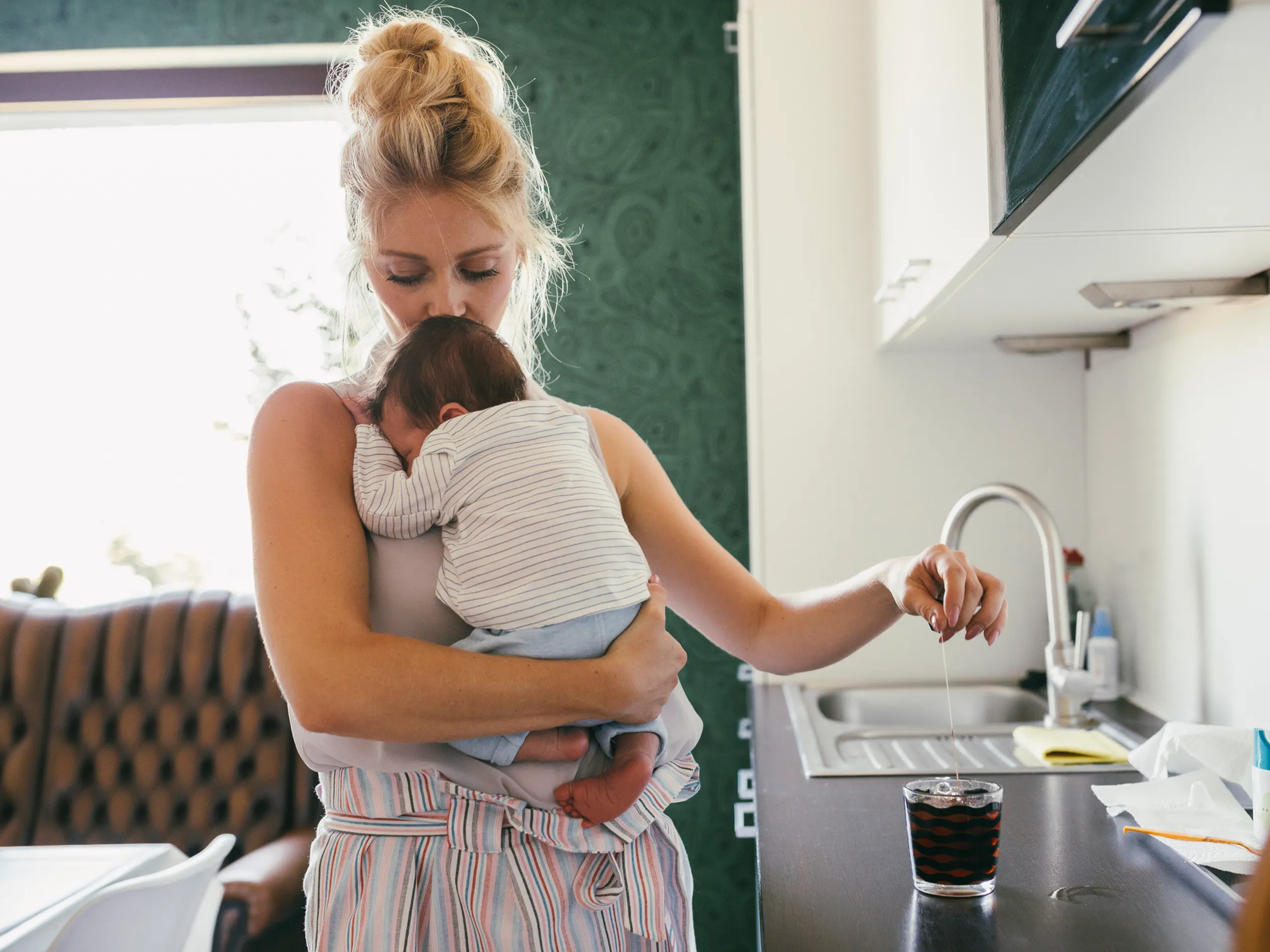 Mutter hält ihr Baby und bereitet Tee in der Küche zu