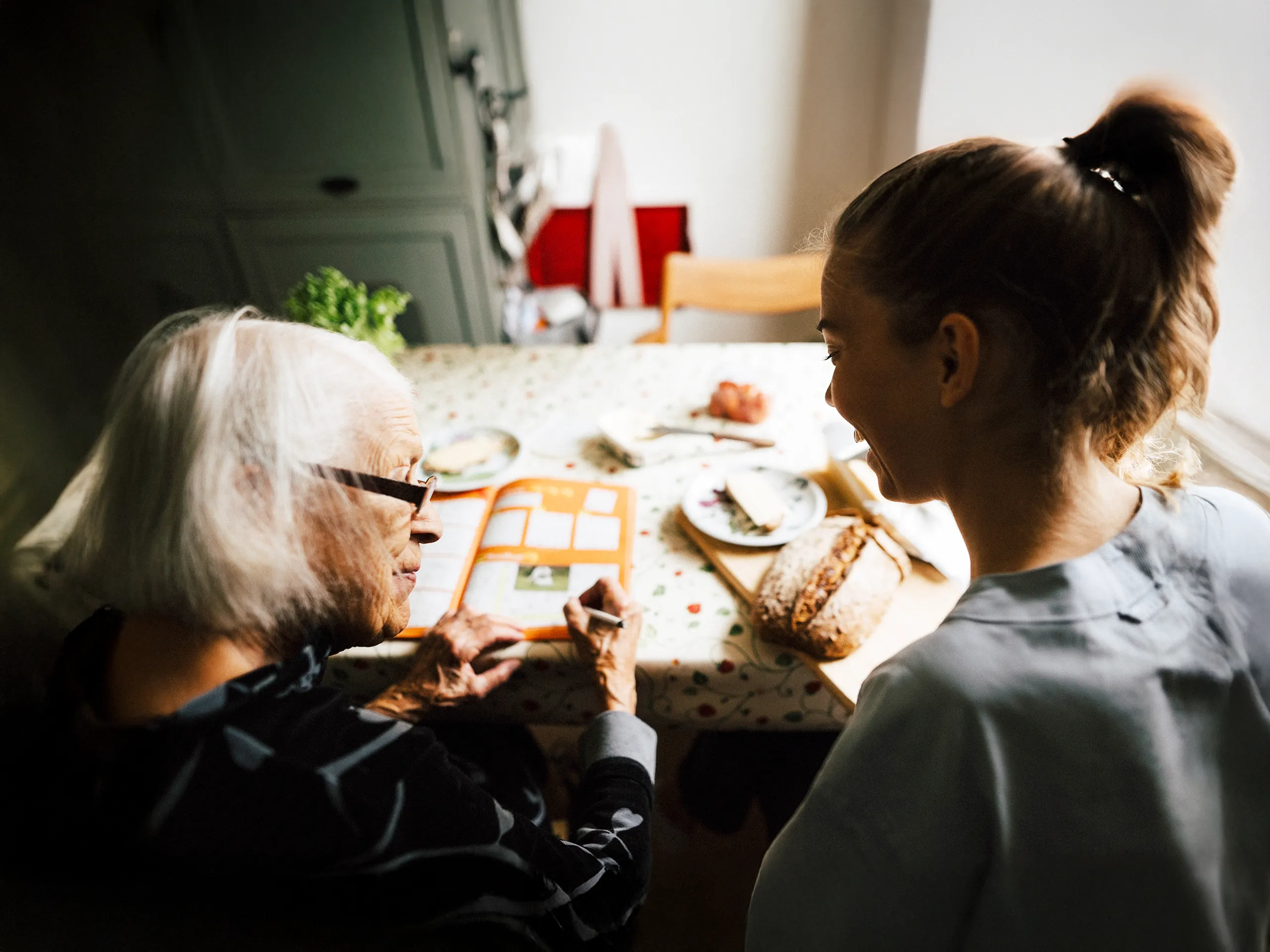 Junge Pflegerin unterhält sich mit Seniorin bei Frühstück
