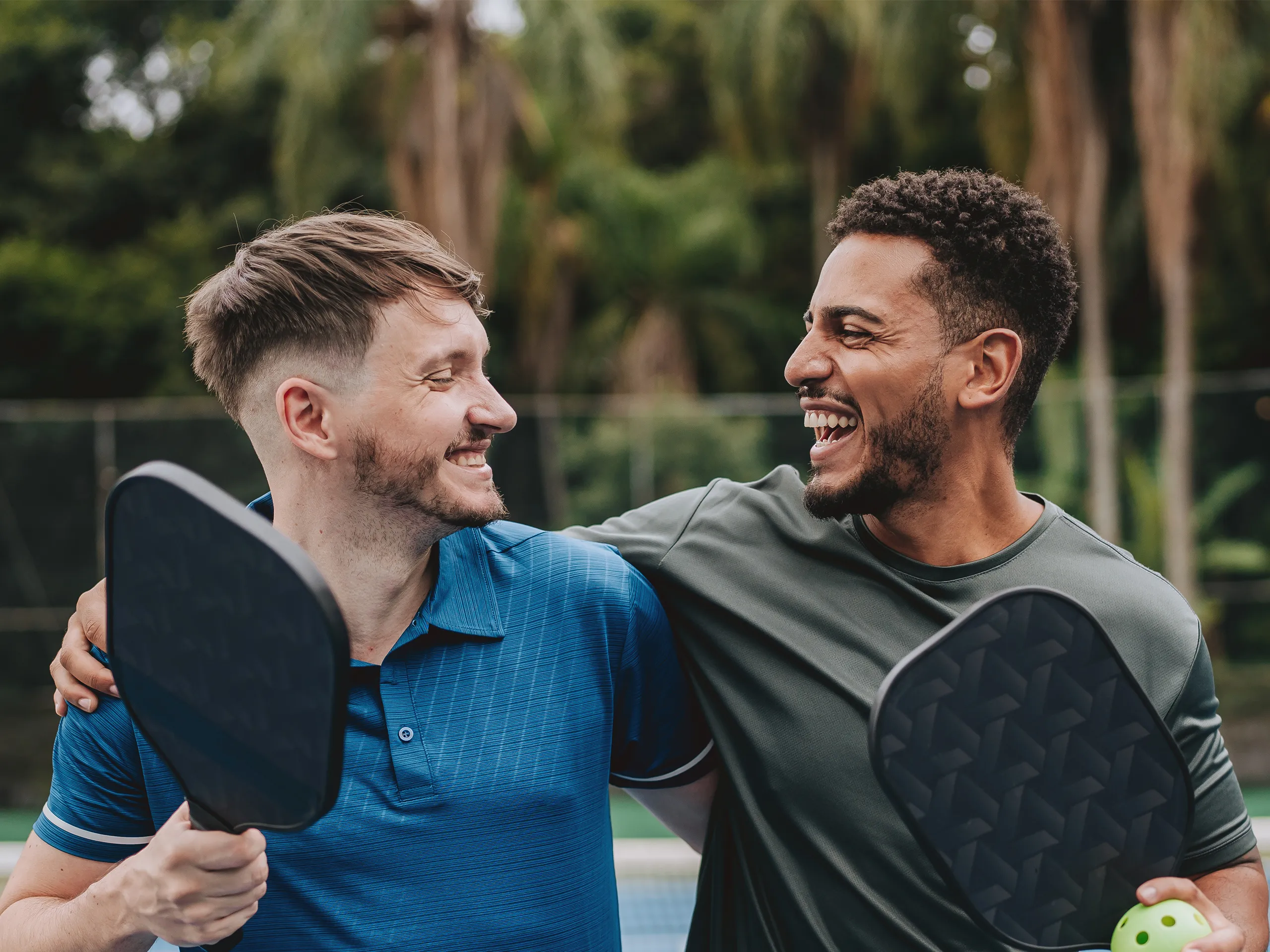 Zwei Männer lächeln und halten Pickleball-Schläger auf einem Spielfeld