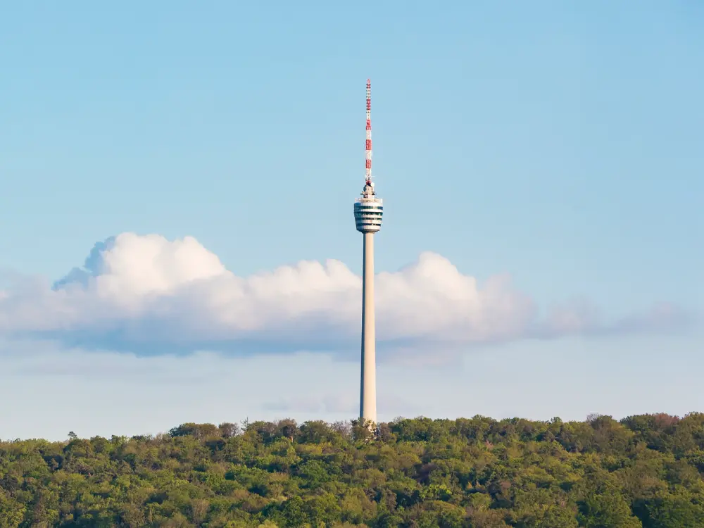 Fernsehturm Stuttgart ragt über bewaldetem Hügel bei blauem Himmel