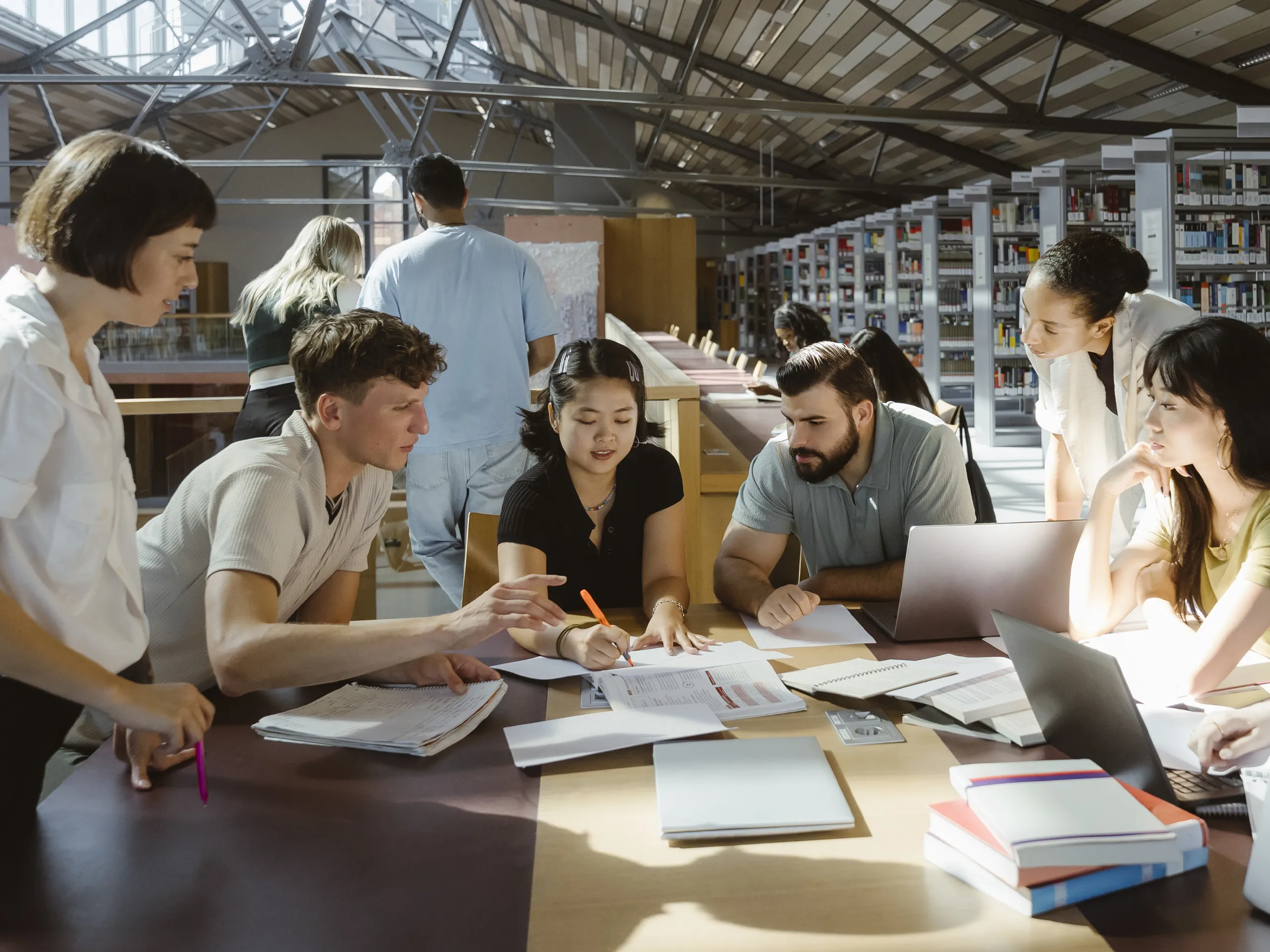 Gruppe junger Menschen arbeitet gemeinsam an Unterlagen in einer Bibliothek
