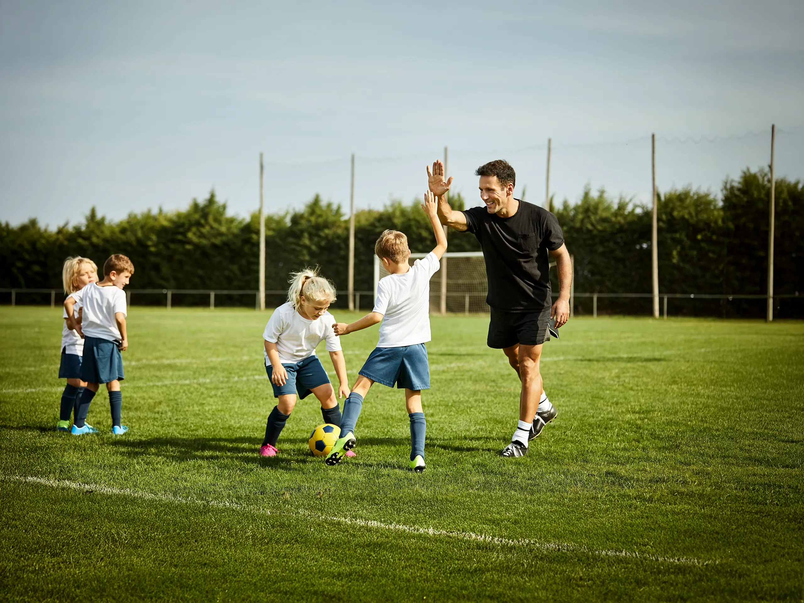 Fußballtrainer gibt Kind ein High-Five auf dem Spielfeld