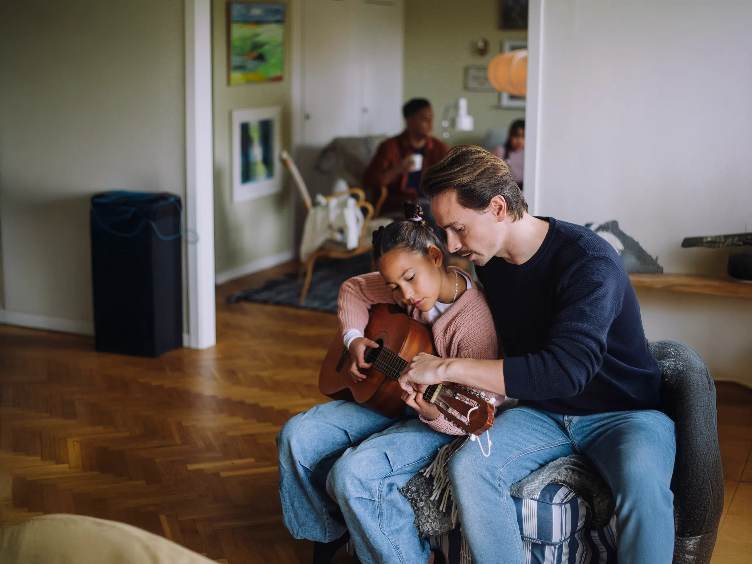 Vater bringt seiner Tochter das Gitarrespielen in einem Wohnzimmer bei