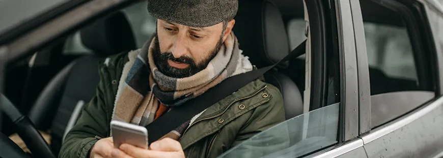 TÜV überziehen? Was Fahrzeughalter zur HU wissen müssen Mann im Auto ließt Infos auf dem Smartphone