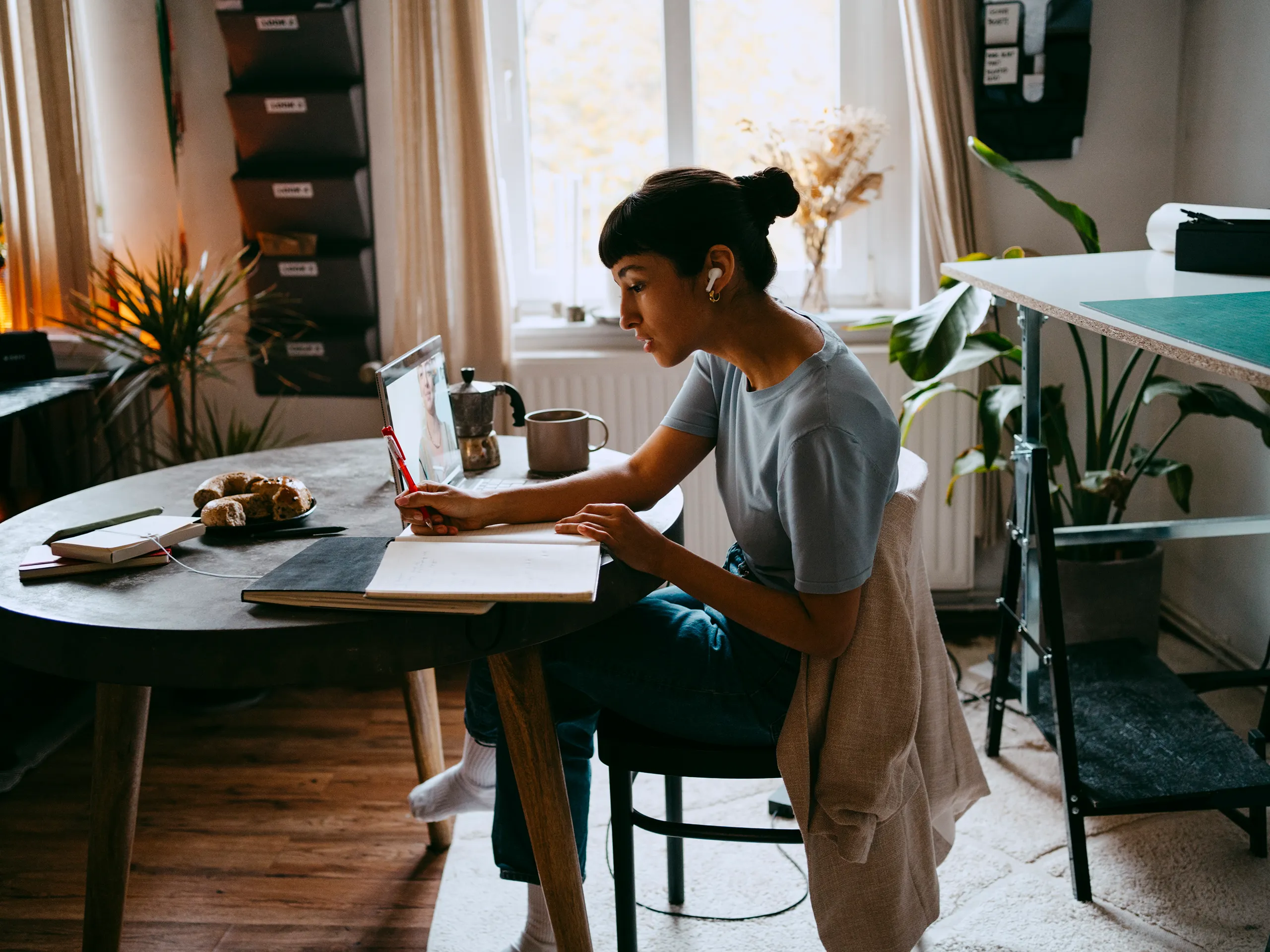 Frau mit Kopfhörern macht Notizen und schaut auf einen Laptop-Bildschirm.
