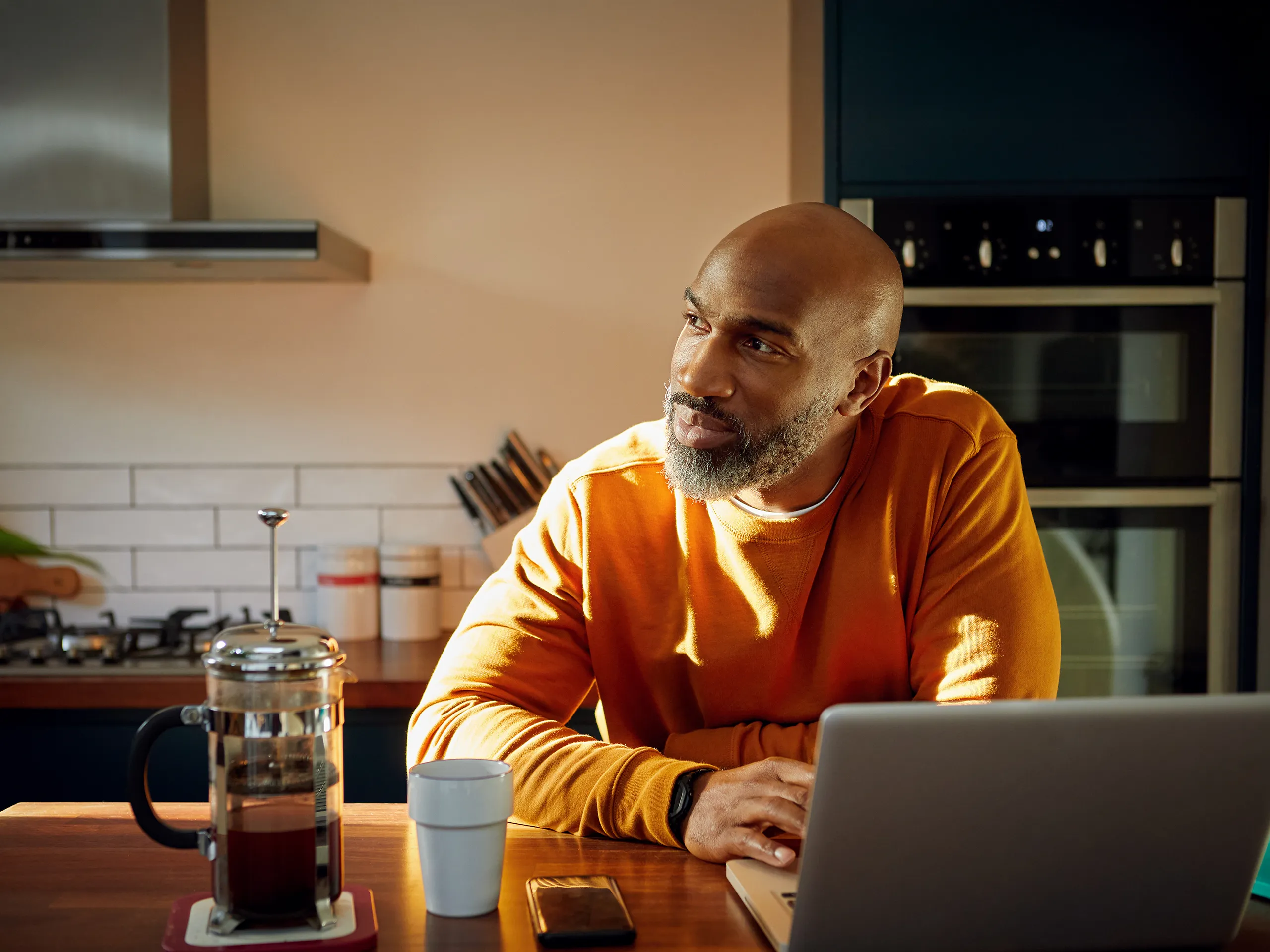 Mann mit Laptop sitzt nachdenklich in der Küche mit Kaffee.