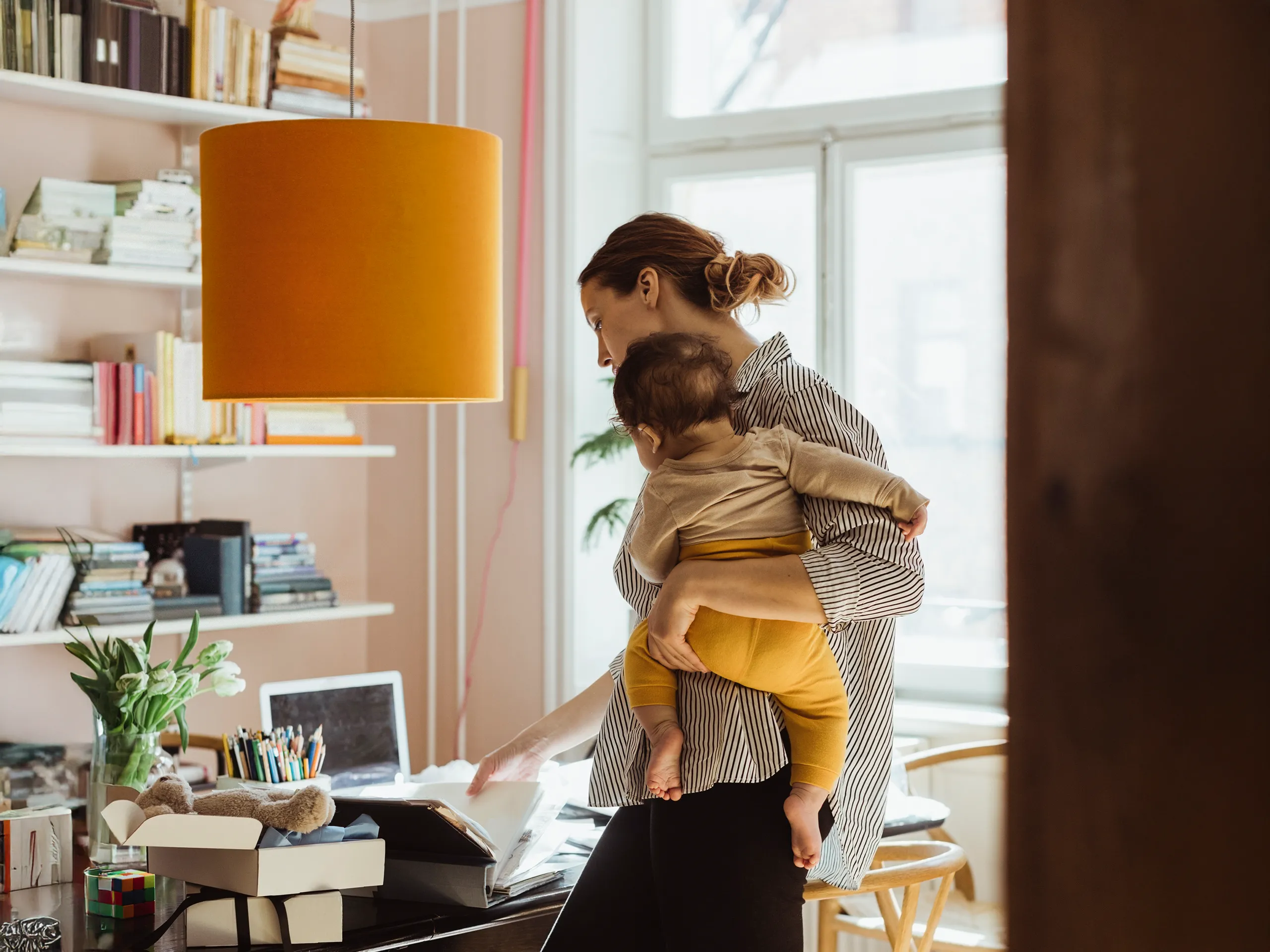 Mutter arbeitet an einem Schreibtisch und hält ihr Baby im Arm