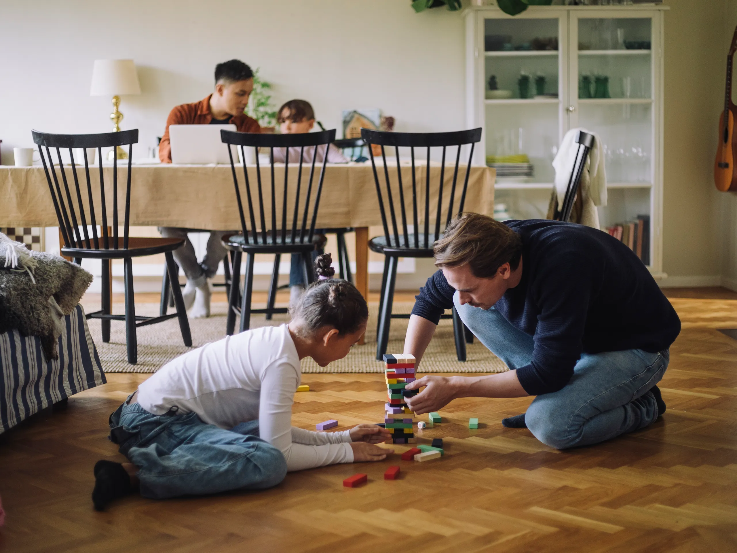 Vater und Tochter bauen gemeinsam einen Turm aus bunten Holzklötzen im Wohnzimmer.